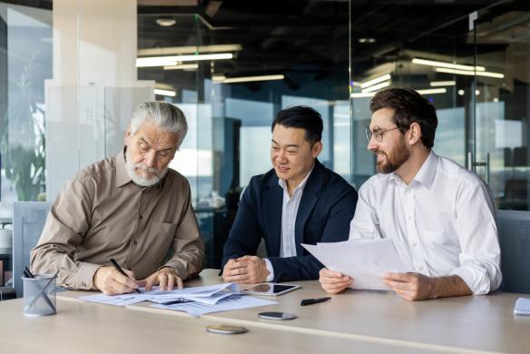 Three businessmen collaborating on financial documents in a bright office environment
