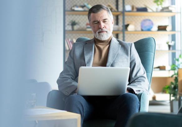 Mature businessman sitting in a plush office chair working on a laptop.