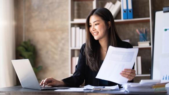 A businesswoman works diligently at her desk, reviewing financial documents and analyzing investment data.