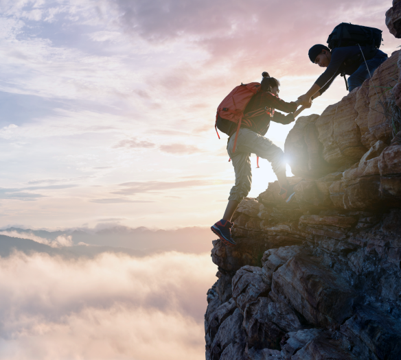 Two climbers reaching the top of a mountain peak at sunrise. 