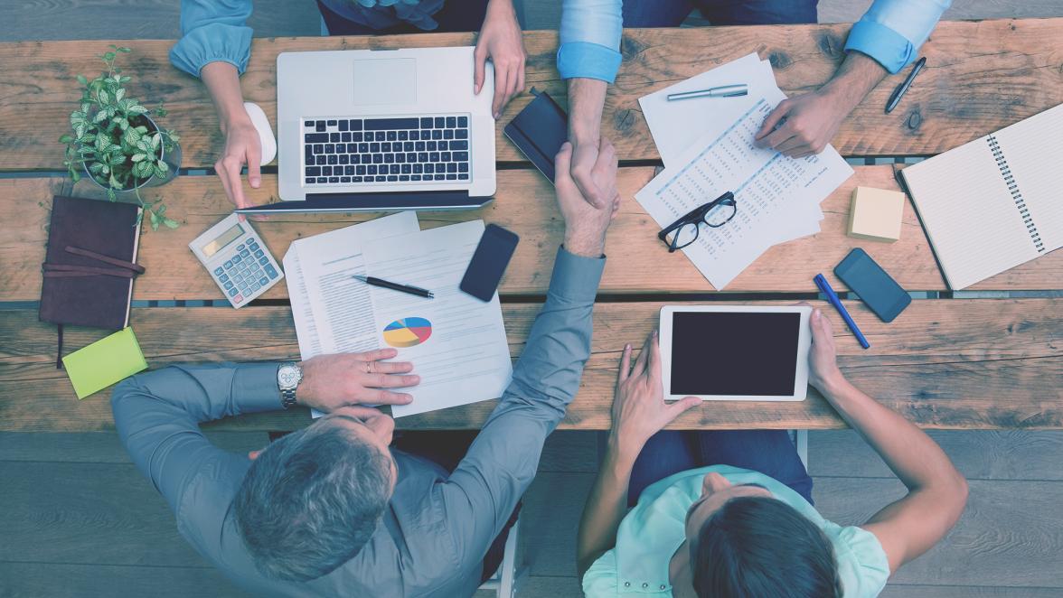 High angle view of businesspeople shaking hands and closing a deal. Successful business teamwork working at the office. Business partners sitting at table and planning work.