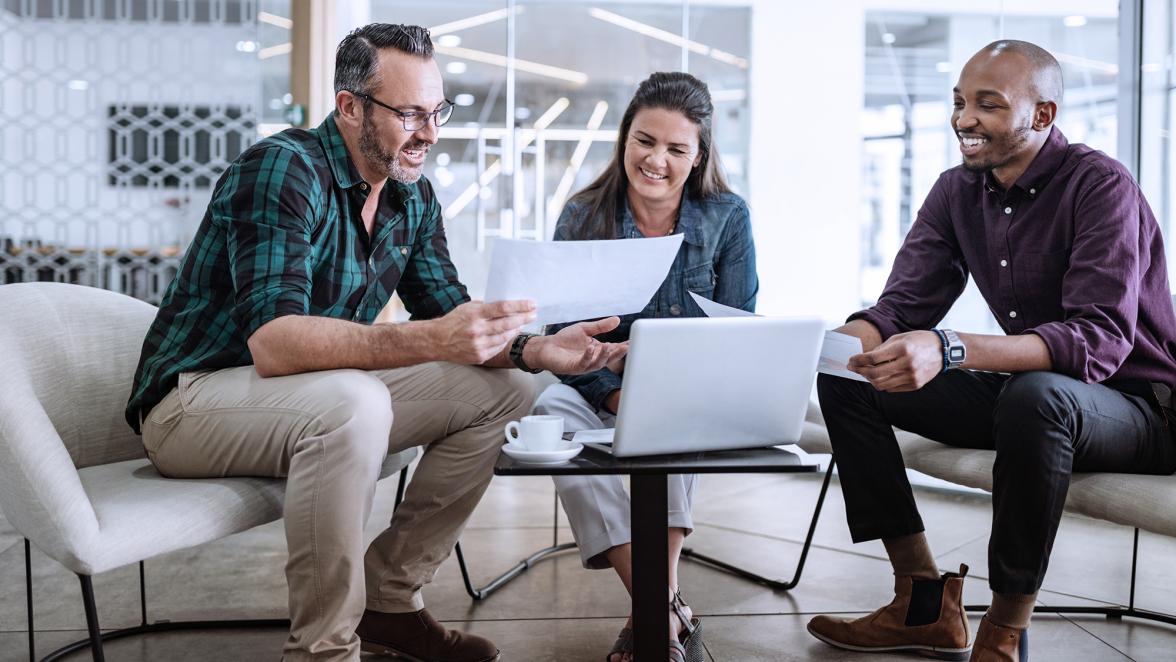 Three smiling diverse business colleagues having casual sit down business strategy meeting.