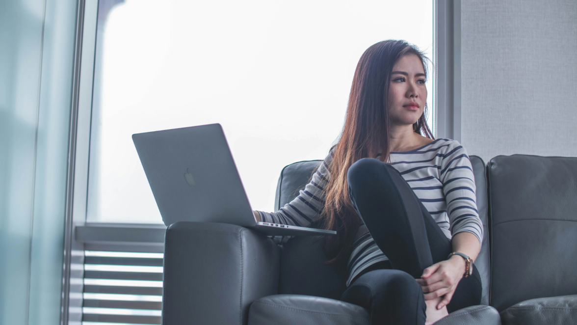 Woman on couch looking away from laptop