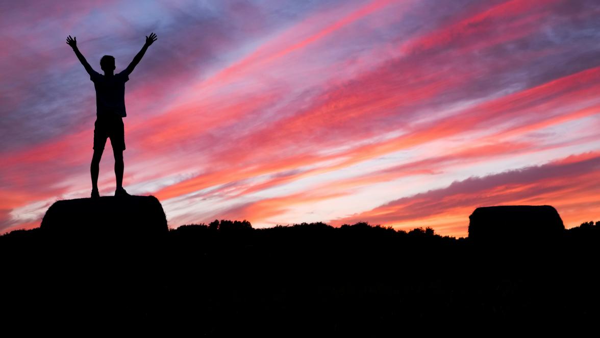 Hiker with raised arms watching a sunset