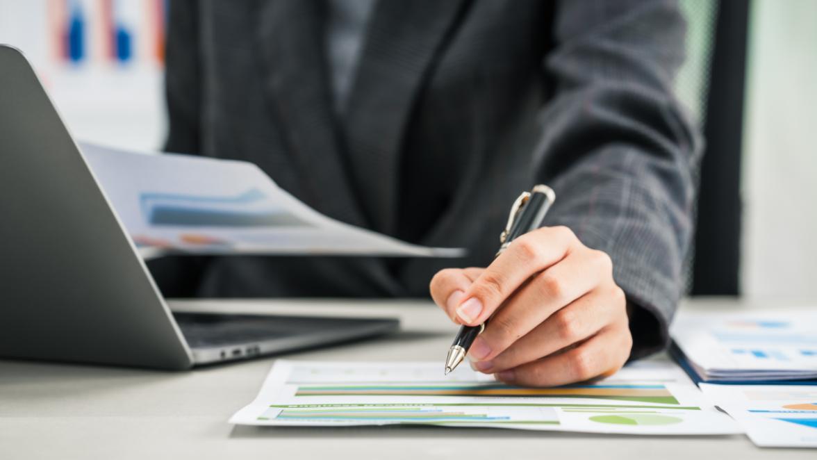 A businesswoman works diligently at her desk, reviewing financial documents and analyzing investment data.