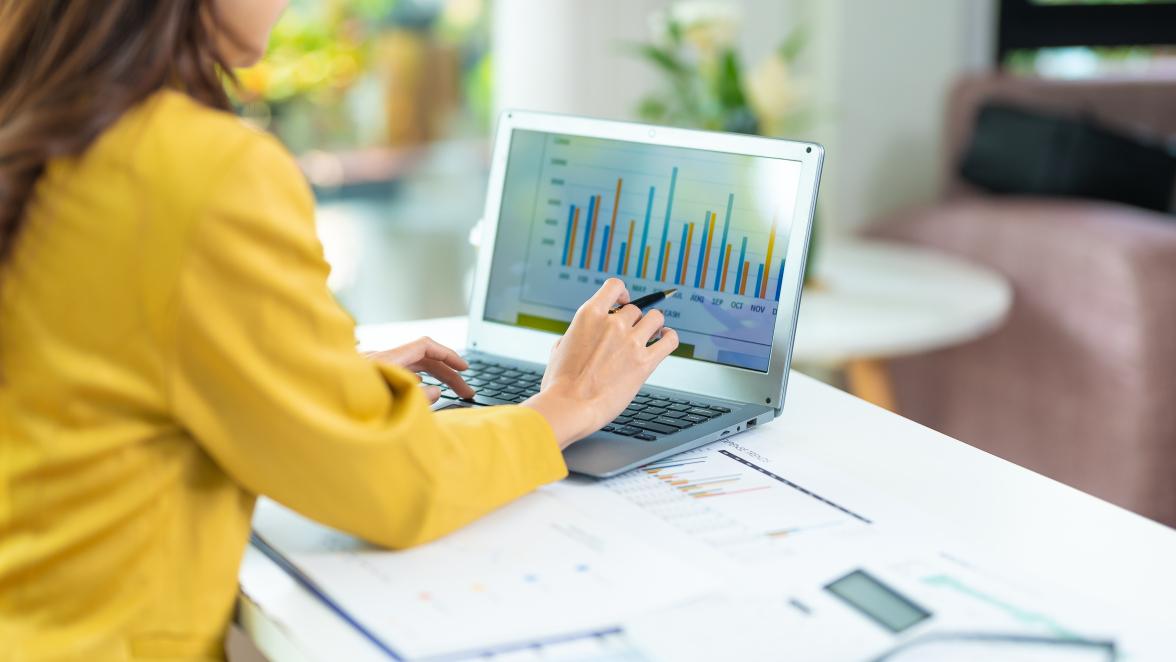 A woman wearing a yellow sweater reviews charts on her laptop