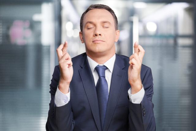 American young hopeful man in office with crossing fingers praying says prayer hopes for future possibility, hope faith concept.