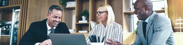 Laughing group of diverse businesspeople going over paperwork and working on a laptop together during an office meeting