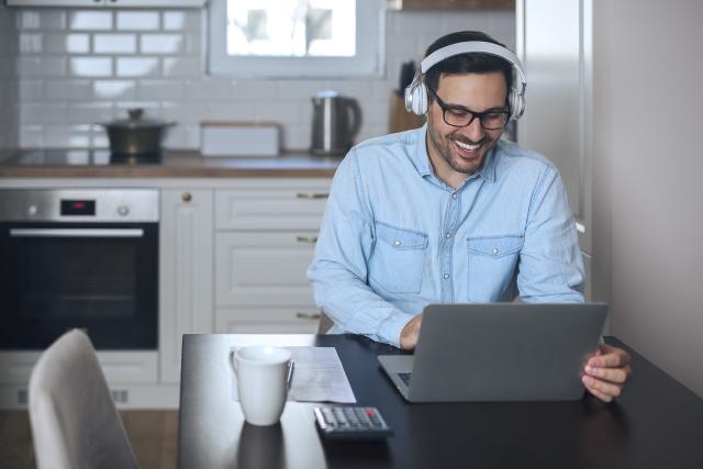 A young businessman working remotely and typing on laptop while listening music on headset.