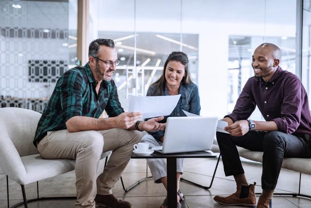 Three smiling diverse business colleagues having casual sit down business strategy meeting.