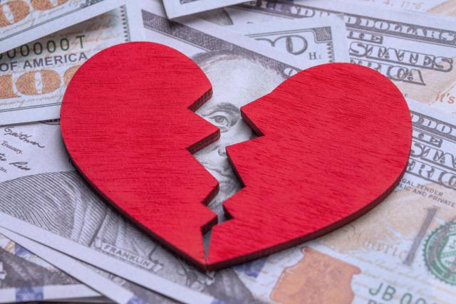 Broken heart because of money. Heart on a stack of cash dollars. Crack in the red heart, Breaking the relationship.