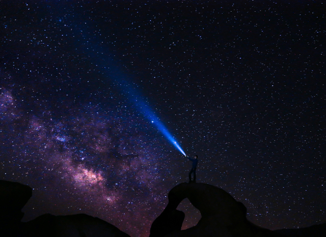 Hiker pointing a flashlight into the Milky Way