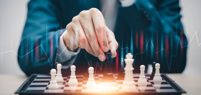 Businessman in a suit plays chess with a chart superimposed above the pieces