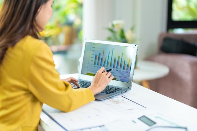 A woman wearing a yellow sweater reviews charts on her laptop