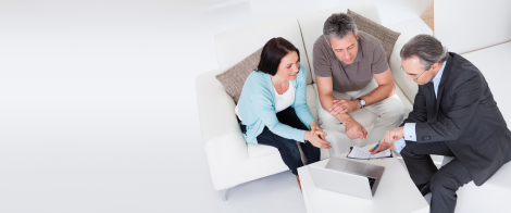 Financial advisor meeting with a couple in a modern, bright setting, discussing documents and reviewing information on a laptop.