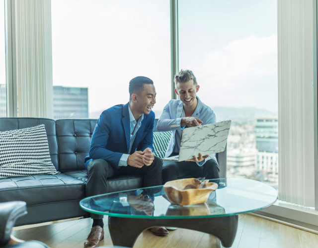 Two men on a couch looking at a laptop