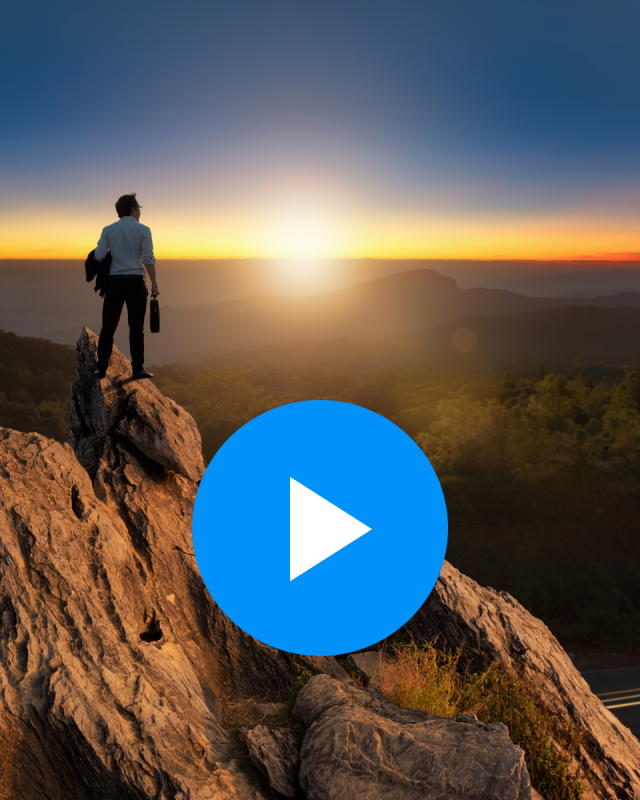 A business professional holding a jacket and a briefcase stands on a tall mountaintop overlooking a vast forest at sunset overlaid by a play button indicating a video.