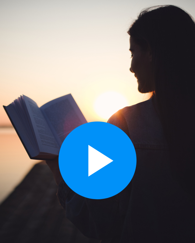 A woman in silhouette reads a book at sunset with a play button overlaid on top indicating a video. 