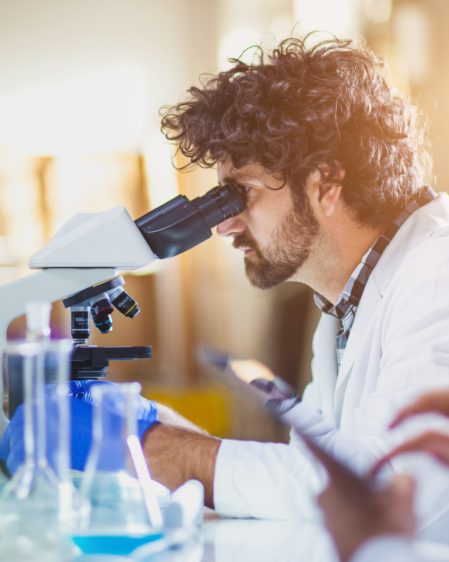 A scientist in a lab looks through a microscope