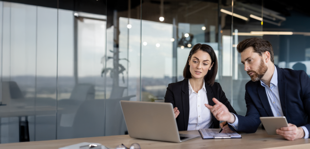 Business colleagues engaged in discussion over project ideas. Man holding tablet , woman pointing at laptop screen.