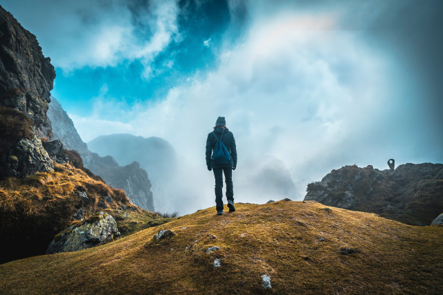 A man standing on a rocky mountain overlooking foggy mountain peaks