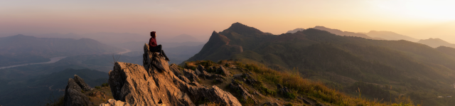 Mountain landscape at sunset; a woman sits atop the peak