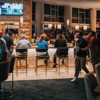 A view from behind of professionals sitting at a bar as other patrons walk past