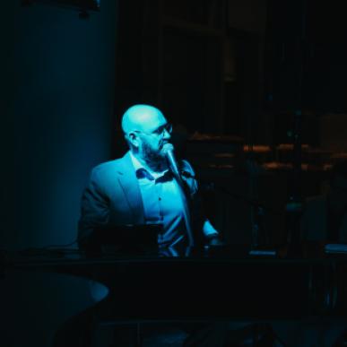 A piano player sings under a blue, hazy light