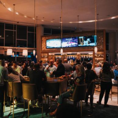 A large group of people gather around tables at an upscale bar