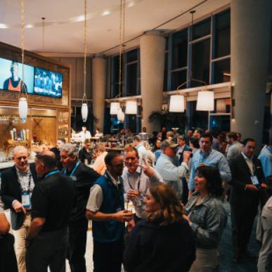 A crowd of professionals enjoy each other's company at an upscale dimly lit bar