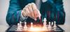 Businessman in a suit plays chess with a chart superimposed above the pieces